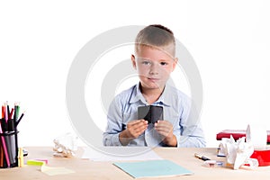 Cute little school boy with sad face sitting at his desk on whit