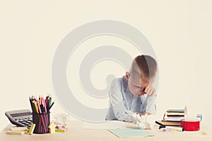 Cute little school boy with sad face sitting at his desk on white background.Unhappy intelligent children in shirt with blue eyes