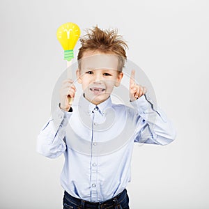 Cute little school boy with yellow paper lightbulb against a white background. Cheerful smiling Kid with funny photo props.