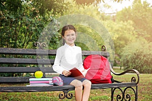 Cute little school child with stationery reading book