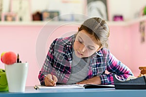 Cute little school girl studying at home in her room. Girl doing homework at home.