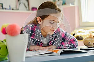 Cute little school girl studying at home in her room. Girl doing homework at home.