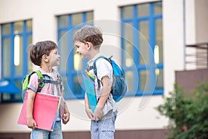 Cute little school students briskly talk on the schoolyard. Children have a good mood. Warm spring morning.