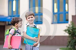 Cute little school students briskly talk on the schoolyard. Children have a good mood. Warm spring morning.