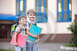 Cute little school students briskly talk on the schoolyard. Children have a good mood. Warm spring morning.