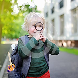 Cute little schoolboy with magnifying glass studying outdoors on sunny day