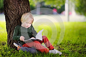 Cute little schoolboy sitting under tree and studying . Back to school concept.