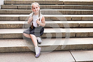 Cute little schoolgirl with bagpack sitting on large stone stairs on warm day photo