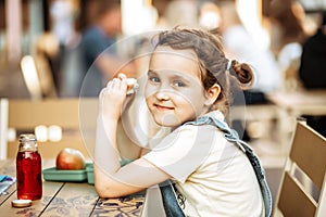 Cute little schoolgirl eating from lunch box outdoor sitting on a school cafe. Food for kids