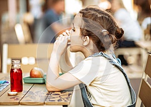 Cute little schoolgirl eating from lunch box outdoor sitting on a school cafe. Food for kids