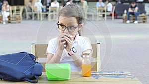 Cute little schoolgirl eating from lunch box outdoor sitting on a school cafeteria. Food for kids