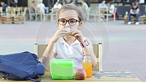 Cute little schoolgirl eating from lunch box outdoor sitting on a school cafeteria. Food for kids