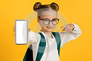 Cute Little Schoolgirl Pointing At Blank Smartphone With White Screen In Hand