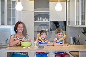 Cute little sibling brother boys cook playing with a banana, as if it were a phone. Mother prepare dough on modern kitchen