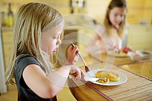 Cute little sisters enjoying their breakfast at home. Pretty children eating pancakes with strawberry sauce before school