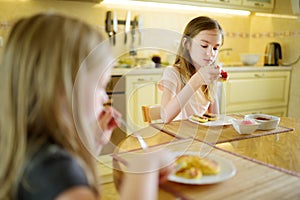 Cute little sisters enjoying their breakfast at home. Pretty children eating pancakes with strawberry sauce before school