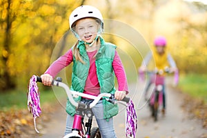 Cute little sisters riding bikes in a city park on sunny autumn day. Active family leisure with kids