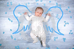 Cute little sleeping baby flying with angel wings over wooden background. Newborn baby with painted angel wings