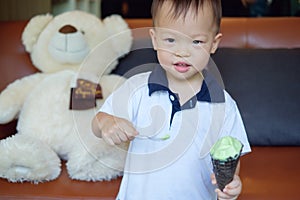 Cute little smiling Asian 1 year old toddler boy child holding spoon and eating soft serve ice cream