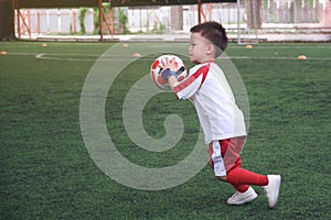 Cute little smiling Asian kindergarten kid, football player in soccer uniform is playing football at Training Session, Soccer