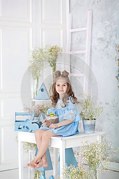 Cute little smiling girl in blue dress sitting on table in kitchen with easter eggs. Easter interior. Spring home decoration. Happ