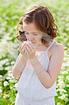 Cute little smiling girl on a chamomile field in spring. Enjoys the scent of daisies with his eyes closed