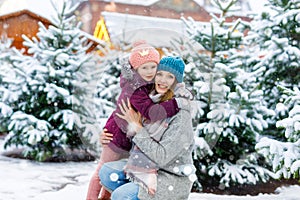 Cute little smiling kid girl and mother on christmas tree market. Happy child, daughter and young woman in winter