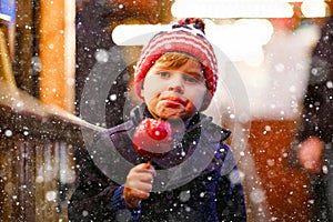 Cute little smiling preschool boy on German Christmas market. Happy child in winter clothes eating sweet sugared glazed