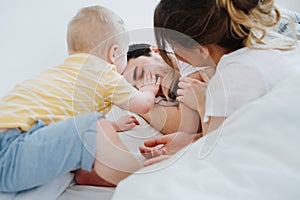 Cute little son along with his mother is trying to wake up his father