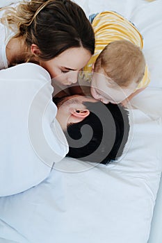 Cute little son along with his mother is trying to wake up his father