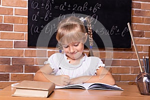 Cute little student girl sitting at a school desk and studying math. The child is doing homework. Preschool education, self