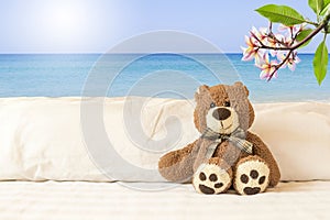 Cute little teddy bear sitting on bed with tropical beach background