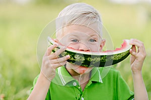 Cute little toddler boy with blond hairs eating watermelon in summergarden photo