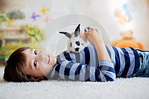 Cute little toddler boy, dressed smart casual, playing with little black and white rabbit