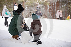 Cute little toddler boy and his mother playing with snow and making snowman. Child having fun outdoors in winter