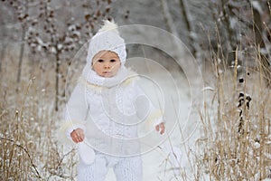 Cute little toddler boy and his older brothers, playing outdoors with snow on a winter day