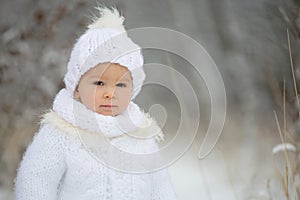 Cute little toddler boy and his older brothers, playing outdoors with snow on a winter day