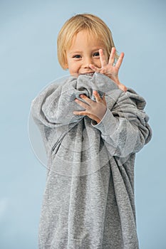 Cute little toddler boy in a huge oversized grey longsleeve over blue