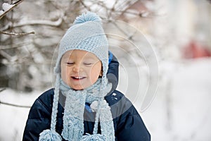 Cute little toddler boy, playing outdoors with snow on a winter day