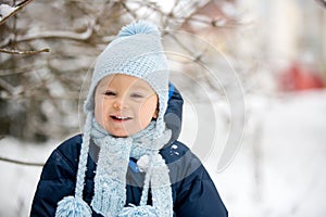 Cute little toddler boy, playing outdoors with snow on a winter day