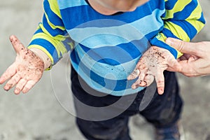 Cute little toddler boy showing mother dirty hands after playing in mud outdoors. Curious child with dirt or soil on