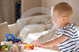 Cute little toddler boy in a striped shirt playing colorful plastic blocks and car sitting on the sofa indoors. child having fun