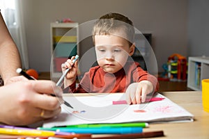 A cute little toddler boy of two years old with dad draws with markers in the album