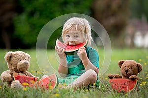 Cute little toddler child, blond boy, eating watermelon in the park