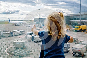 Cute little toddler girl at the airport, traveling. Happy healthy child waiting near window and watching airplanes