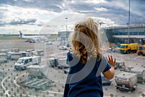 Cute little toddler girl at the airport, traveling. Happy healthy child waiting near window and watching airplanes