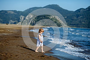 Cute little toddler girl in blue dress runnig and playing on the wild Iztuzu beach, Turkey