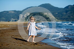 Cute little toddler girl in blue dress runnig and playing on the wild Iztuzu beach, Turkey