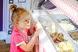 Cute little toddler girl choosing and buying ice cream in a cafe. Happy baby child looking at different sorts of