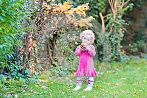 Cute little toddler girl eating apple in garden